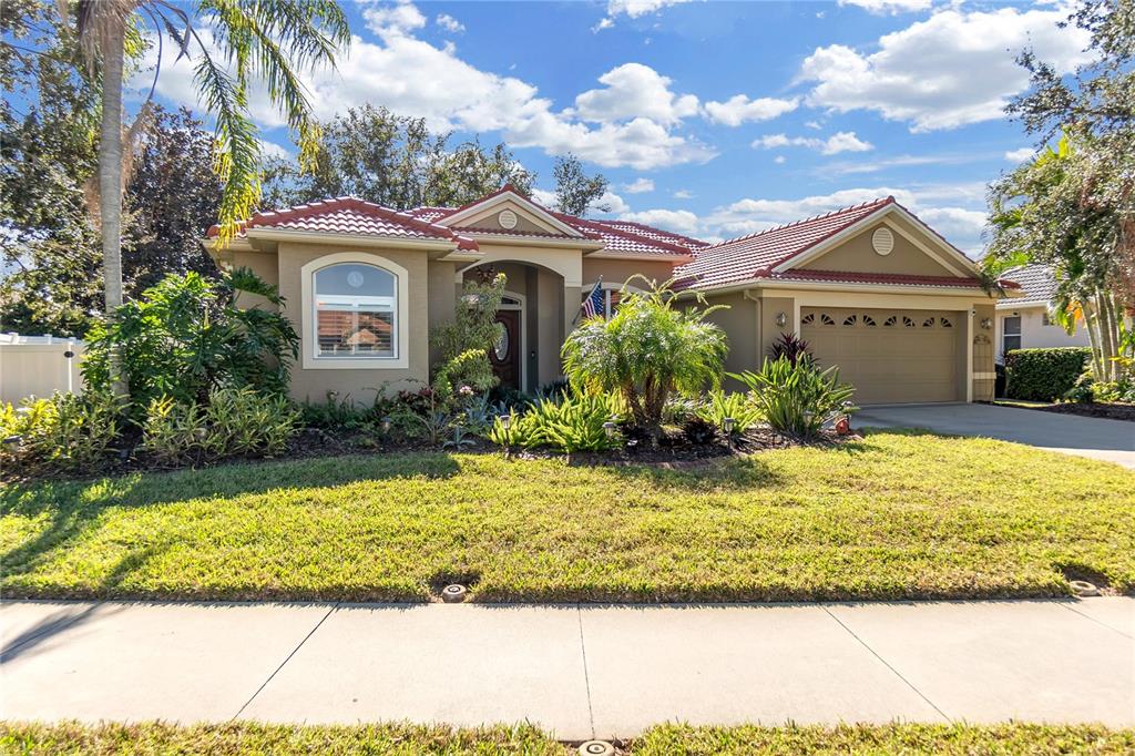 A single-story house with a tan stucco exterior, red tile roof, and a two-car garage — 5723 EASTWIND DRIVE, SARASOTA, FL