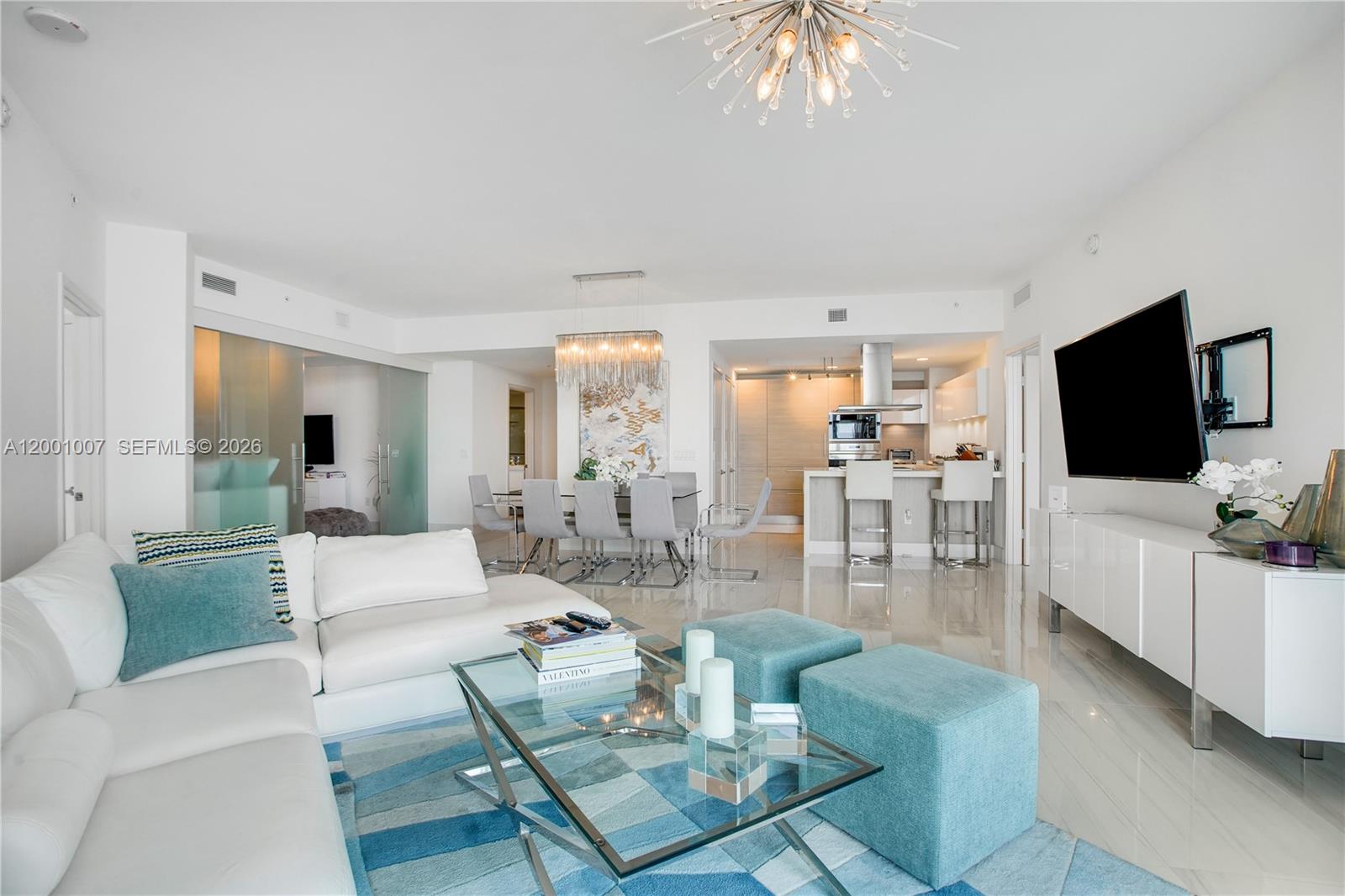 A modern open-concept living and dining area features white furniture, blue accents, and tile flooring — 17111 Biscayne Blvd # 2008, North Miami Beach FL 33160, NORTH MIAMI BEACH, FL