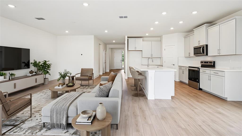 An open-concept living room and kitchen feature white cabinetry, light wood flooring, and modern furniture — 4241 SW 52ND LANE ROAD, OCALA, FL