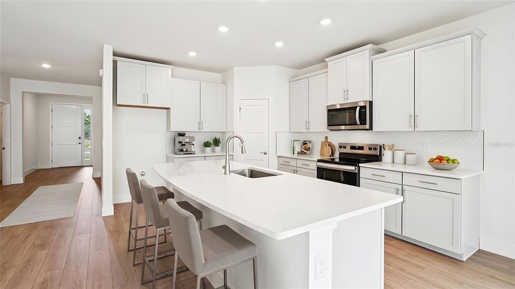 A modern kitchen features white cabinetry, a large central island with seating, and wood flooring — 4241 SW 52ND LANE ROAD, OCALA, FL