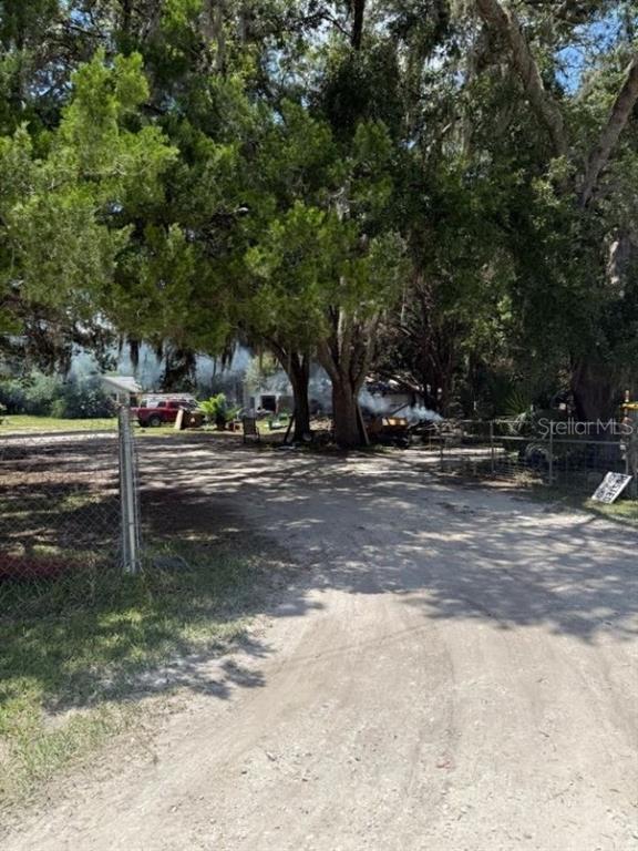 A dirt driveway leads toward a wooded property with a red truck and visible smoke — 4543 COBB ROAD, LAND O LAKES, FL