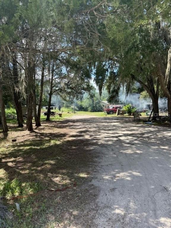 A dirt driveway leads toward a wooded area with a red truck and visible smoke — 4543 COBB ROAD, LAND O LAKES, FL