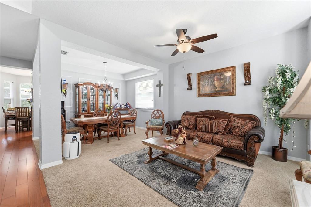A living room with beige carpet, a brown patterned sofa, and an adjacent dining area — 414 MOHAVE TERRACE, LAKE MARY, FL