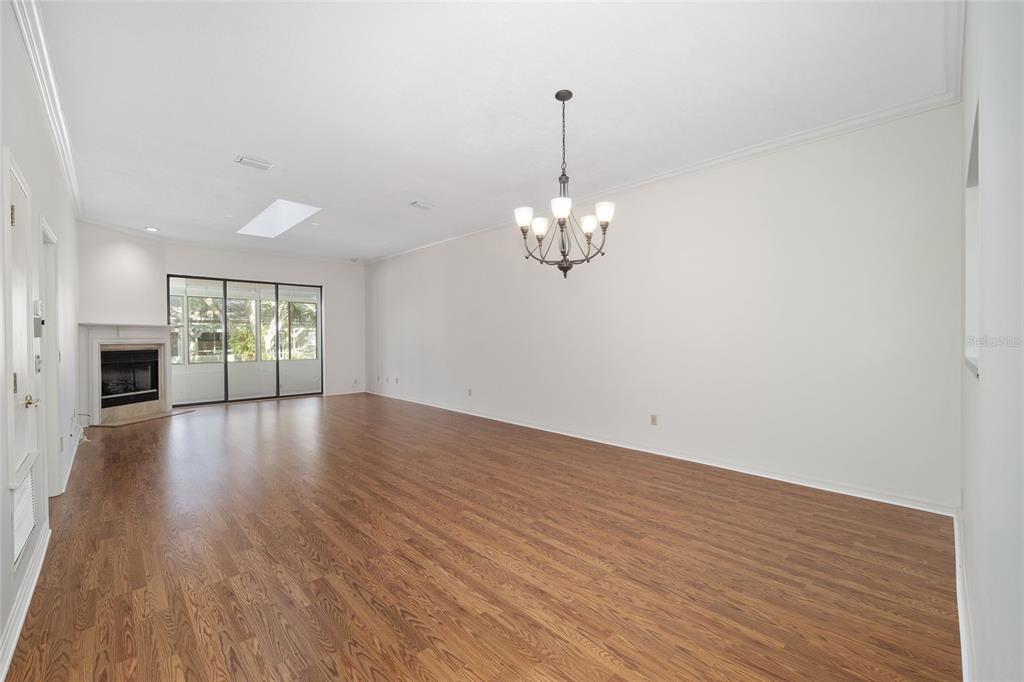 A spacious living room features wood-look flooring, a fireplace, a chandelier, and sliding glass doors — 1906 SE CLATTERBRIDGE ROAD SE, OCALA, FL
