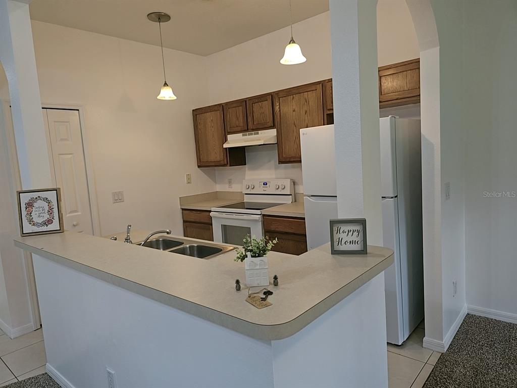 A kitchen features wood cabinets, white appliances, a breakfast bar, and two pendant lights — 1124 N FAIRWAY DRIVE, APOPKA, FL