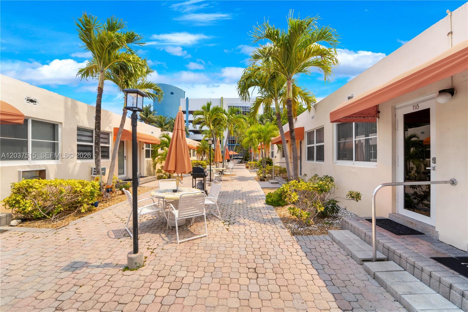 A paved courtyard features outdoor seating, palm trees, and building entrances with awnings — 336 Arthur St # 118, Hollywood FL 33019, HOLLYWOOD, FL