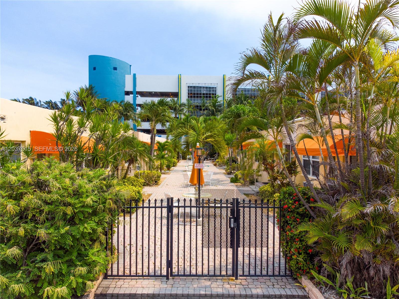 A black metal gate opens to a paved courtyard between two low-rise buildings with awnings — 336 Arthur St # 118, Hollywood FL 33019, HOLLYWOOD, FL