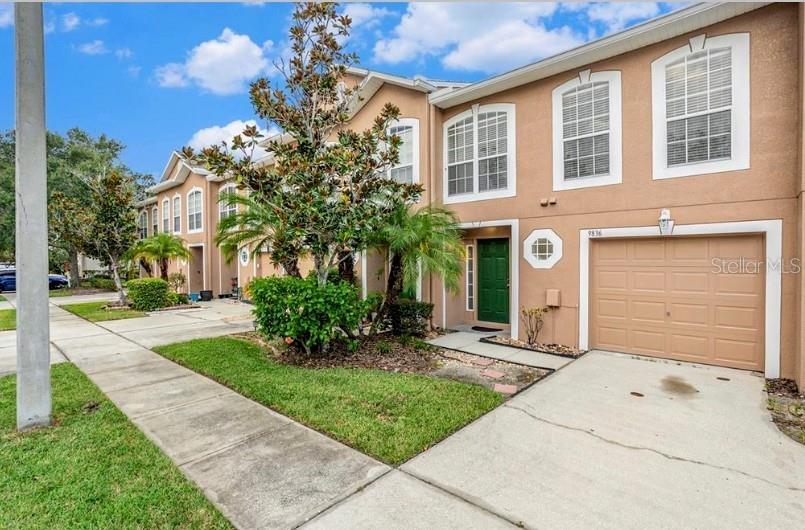 A two-story townhouse with a tan stucco exterior, a green front door, and a garage — 9836 ASHBURN LAKE DRIVE, TAMPA, FL