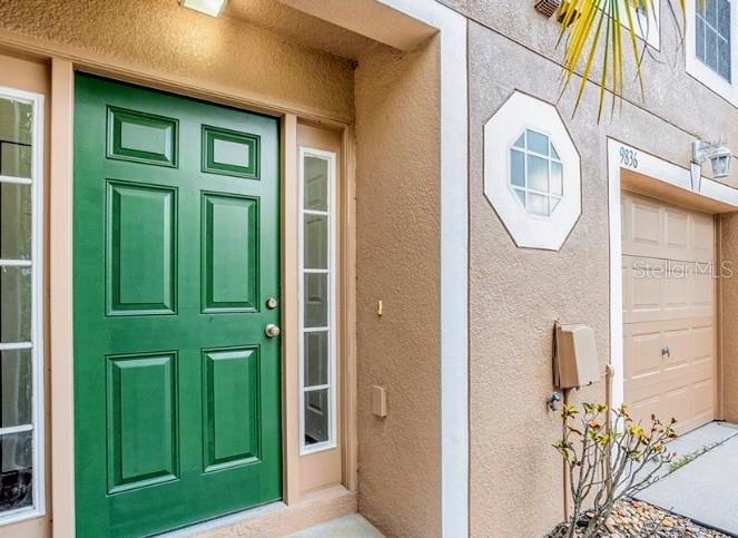 A green front door sits next to a tan garage door on a stucco building — 9836 ASHBURN LAKE DRIVE, TAMPA, FL