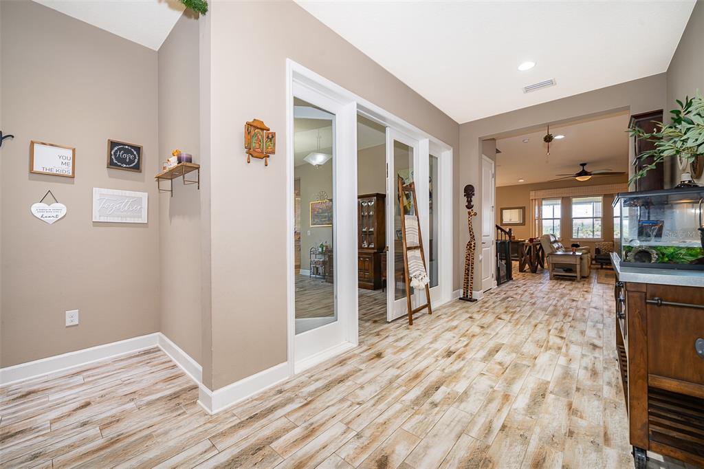A hallway with wood-look tile flooring leads to a living area with glass-paneled doors — 3546 MEDITERRA DRIVE, CLERMONT, FL