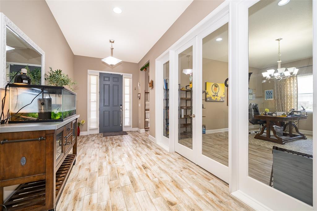 A foyer features wood-look tile flooring, a dark front door, and glass-paneled office doors — 3546 MEDITERRA DRIVE, CLERMONT, FL