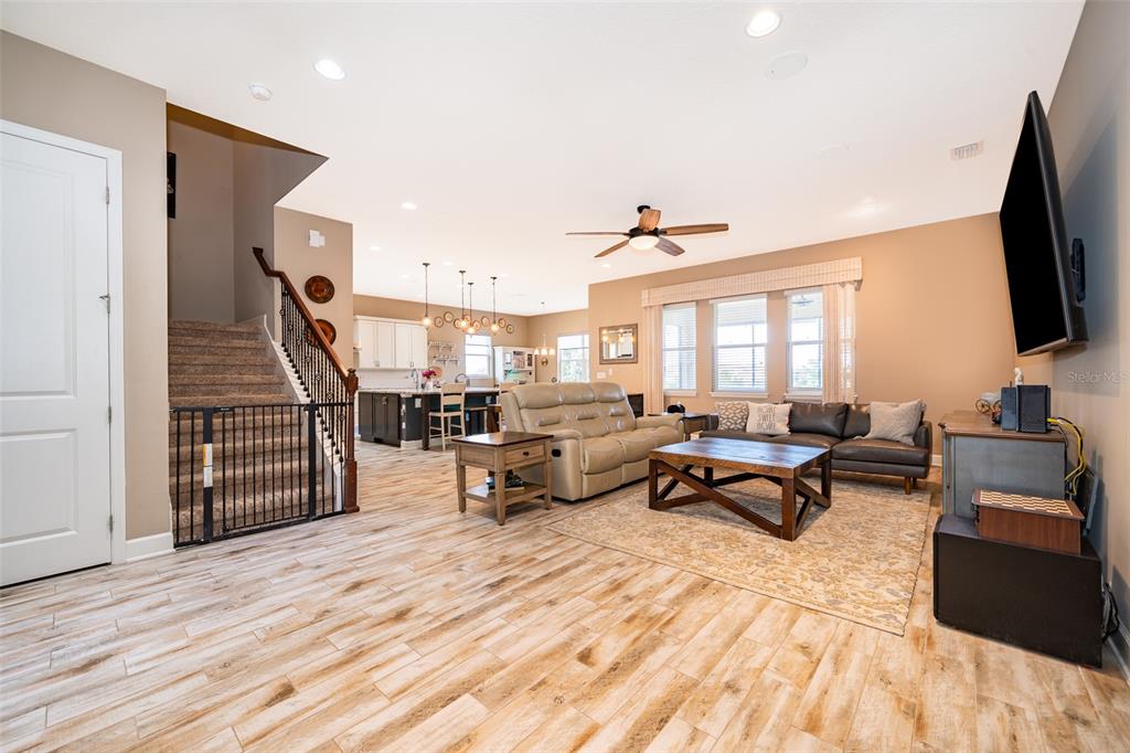 An open-concept living room features wood-look tile flooring, a staircase, and a kitchen in back — 3546 MEDITERRA DRIVE, CLERMONT, FL