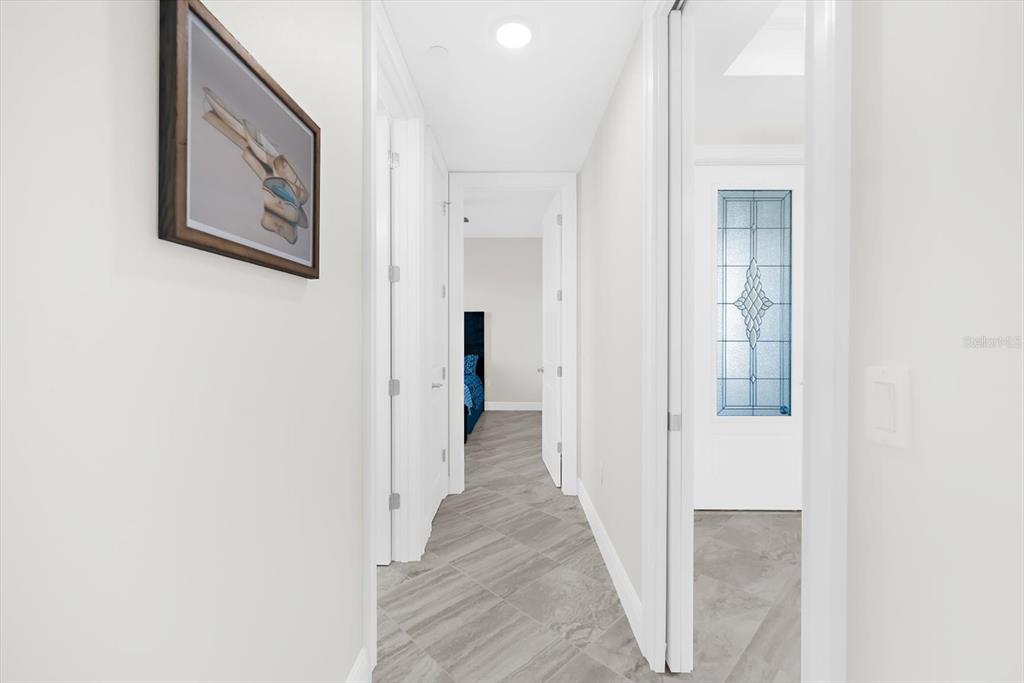 A hallway with gray tile flooring leads to a bedroom and a glass-paneled door — 507 TAMIAMI TRAIL N UNIT 602, VENICE, FL