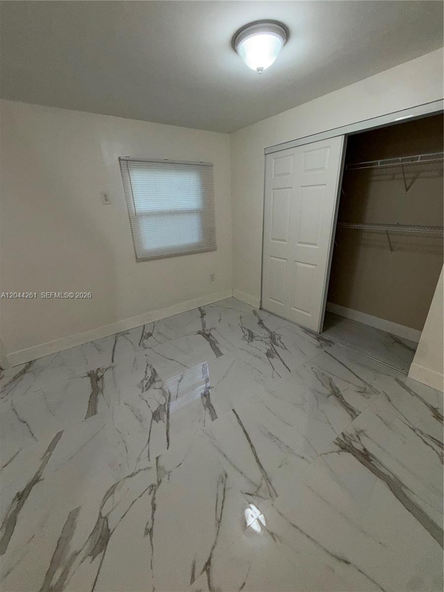 A small bedroom features white walls, a sliding closet door, and white marble-patterned tile flooring — 6497 W 8th Ln # 6497, Hialeah FL 33012, HIALEAH, FL