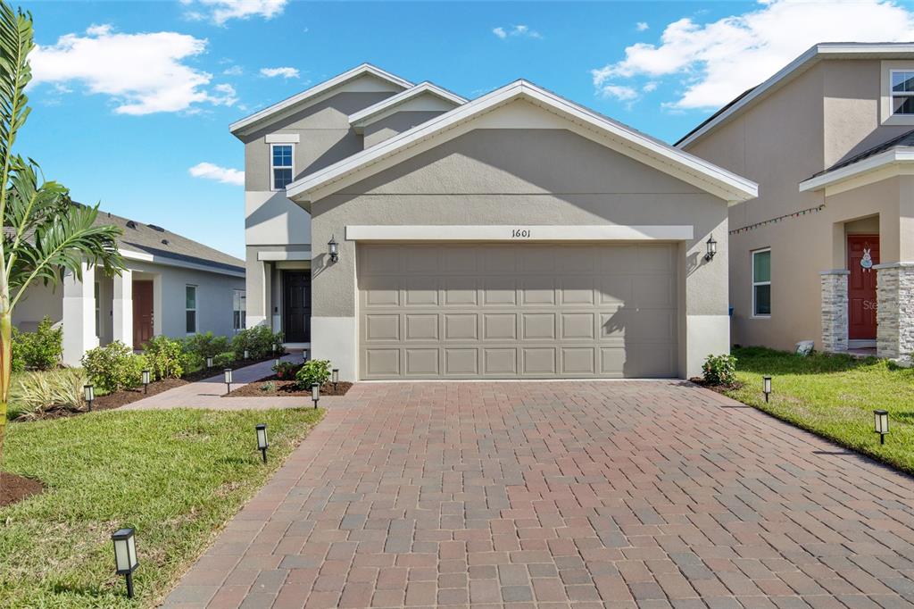 A two-story suburban house features a tan stucco exterior, a brick paver driveway, and a garage — 1601 SWAN SWIM DRIVE, DAVENPORT, FL