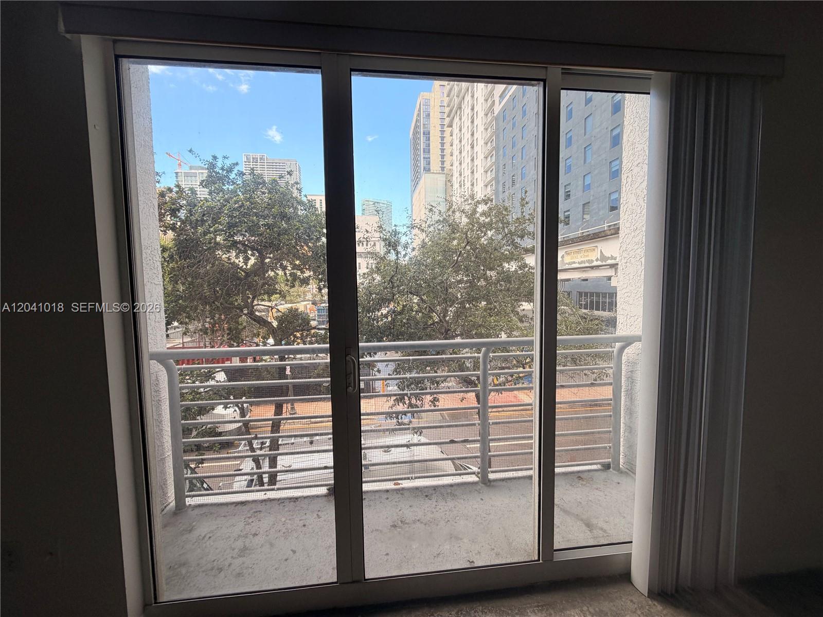 A sliding glass door opens to a balcony overlooking city buildings and trees — 133 NE 2nd Ave # 209, Miami FL 33132, MIAMI, FL