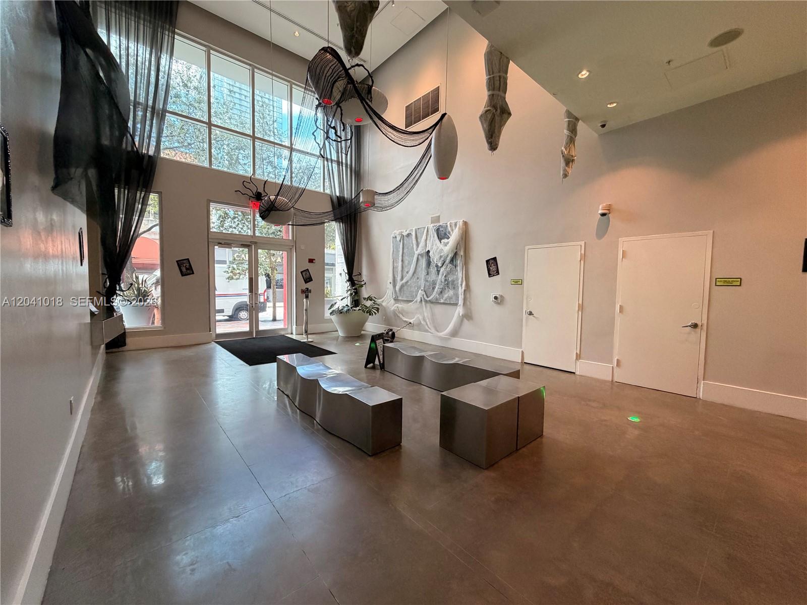 A modern lobby features high ceilings, concrete floors, metal benches, and Halloween-themed decorations — 133 NE 2nd Ave # 209, Miami FL 33132, MIAMI, FL