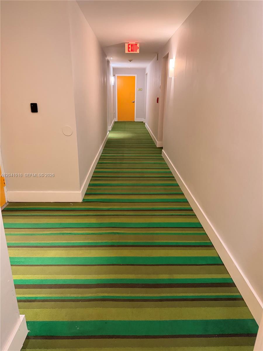A long hallway features striped green carpeting, light-colored walls, and a bright orange door — 133 NE 2nd Ave # 209, Miami FL 33132, MIAMI, FL