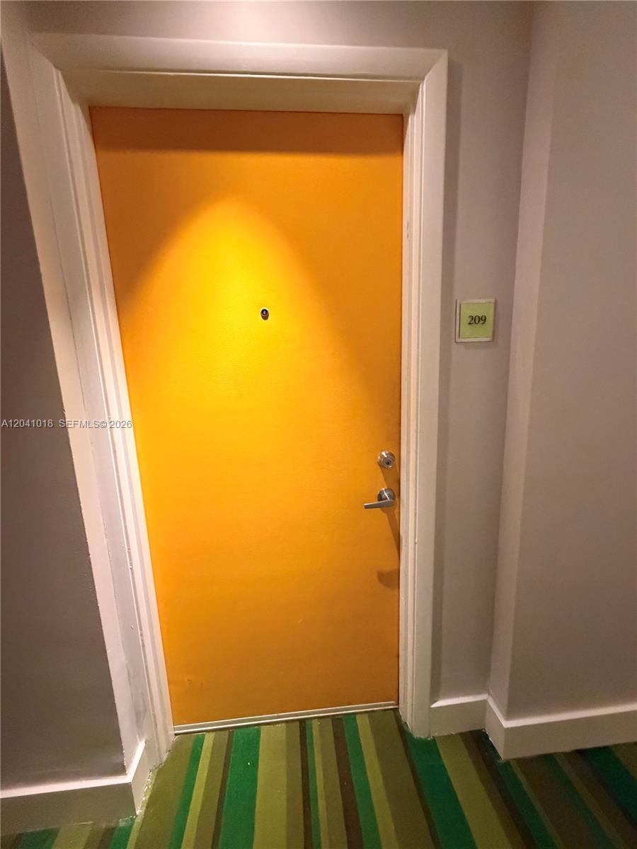 A bright orange door with a peephole and a room number sign in a hallway — 133 NE 2nd Ave # 209, Miami FL 33132, MIAMI, FL