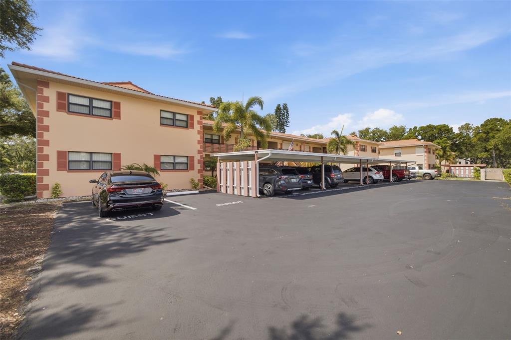 An exterior view of a multi-story apartment building with a parking lot and covered carports — 8140 TERRACE GARDEN DRIVE UNIT 103, ST PETERSBURG, FL