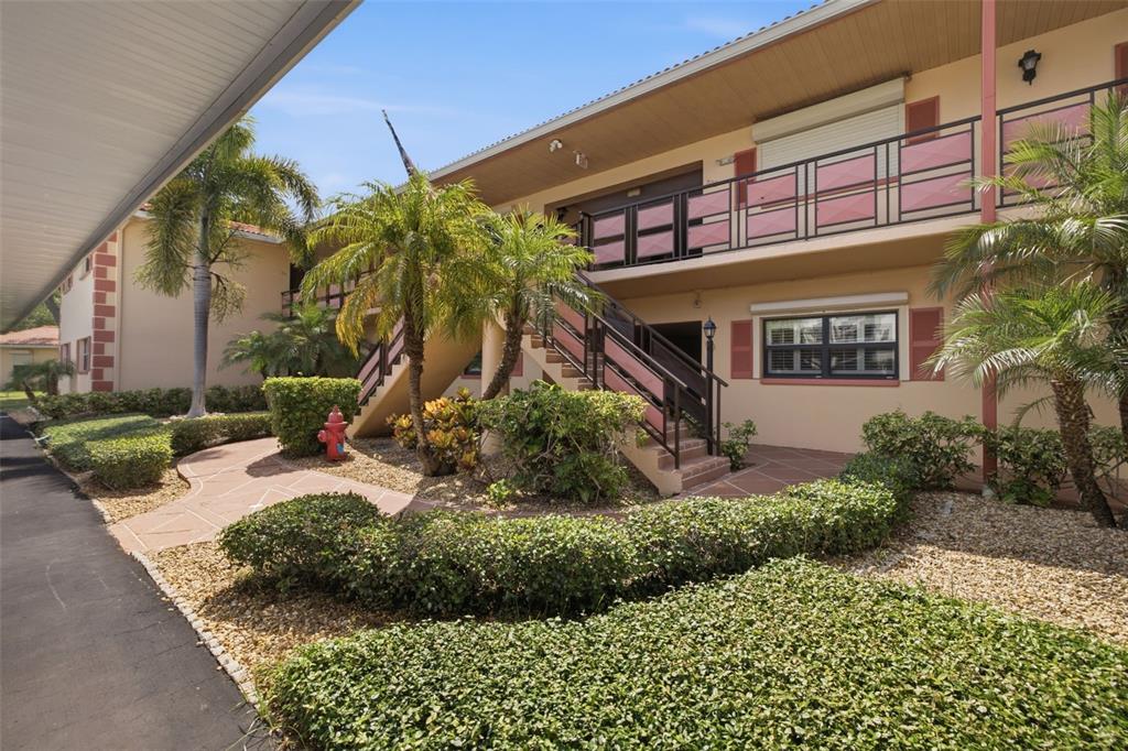 An exterior view of a two-story apartment building with stairs, palm trees, and landscaping — 8140 TERRACE GARDEN DRIVE UNIT 103, ST PETERSBURG, FL