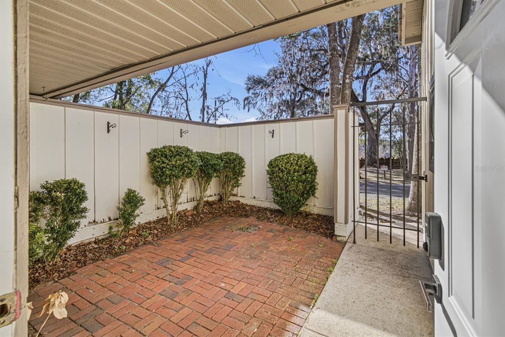 A brick-paved patio area features a white privacy fence, small shrubs, and a metal gate — 5528 SW 4TH PLACE UNIT 5528, GAINESVILLE, FL