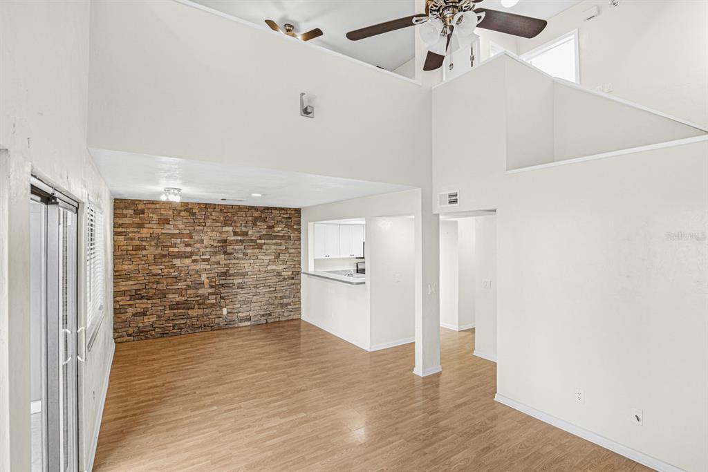 A living room with wood-look flooring, a stone accent wall, and a high vaulted ceiling — 5528 SW 4TH PLACE UNIT 5528, GAINESVILLE, FL