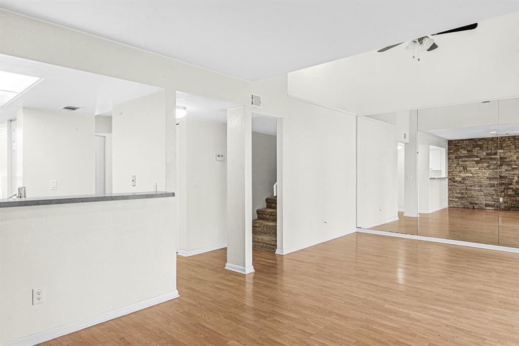 A living room with light wood floors, white walls, a mirrored wall, and carpeted stairs — 5528 SW 4TH PLACE UNIT 5528, GAINESVILLE, FL