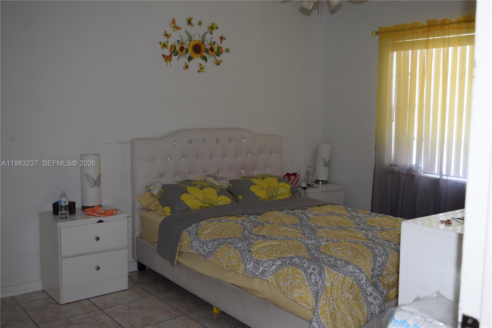 A bedroom features a tufted headboard, yellow and gray bedding, and a window with curtains — 1335 W 68th St # 106, Hialeah FL 33014, HIALEAH, FL