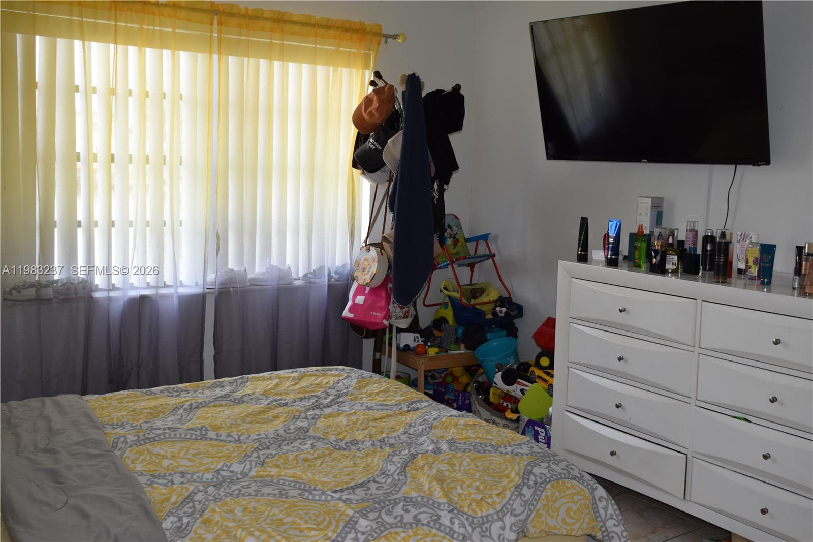 A bedroom features a bed with a yellow patterned comforter, a dresser, and a wall-mounted television — 1335 W 68th St # 106, Hialeah FL 33014, HIALEAH, FL