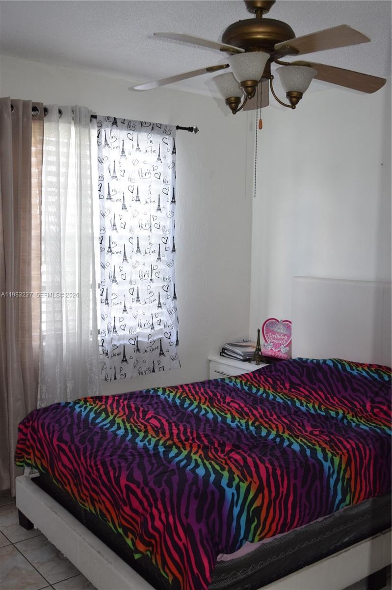 A bedroom features a bed with a colorful zebra-print comforter, a ceiling fan, and patterned curtains — 1335 W 68th St # 106, Hialeah FL 33014, HIALEAH, FL