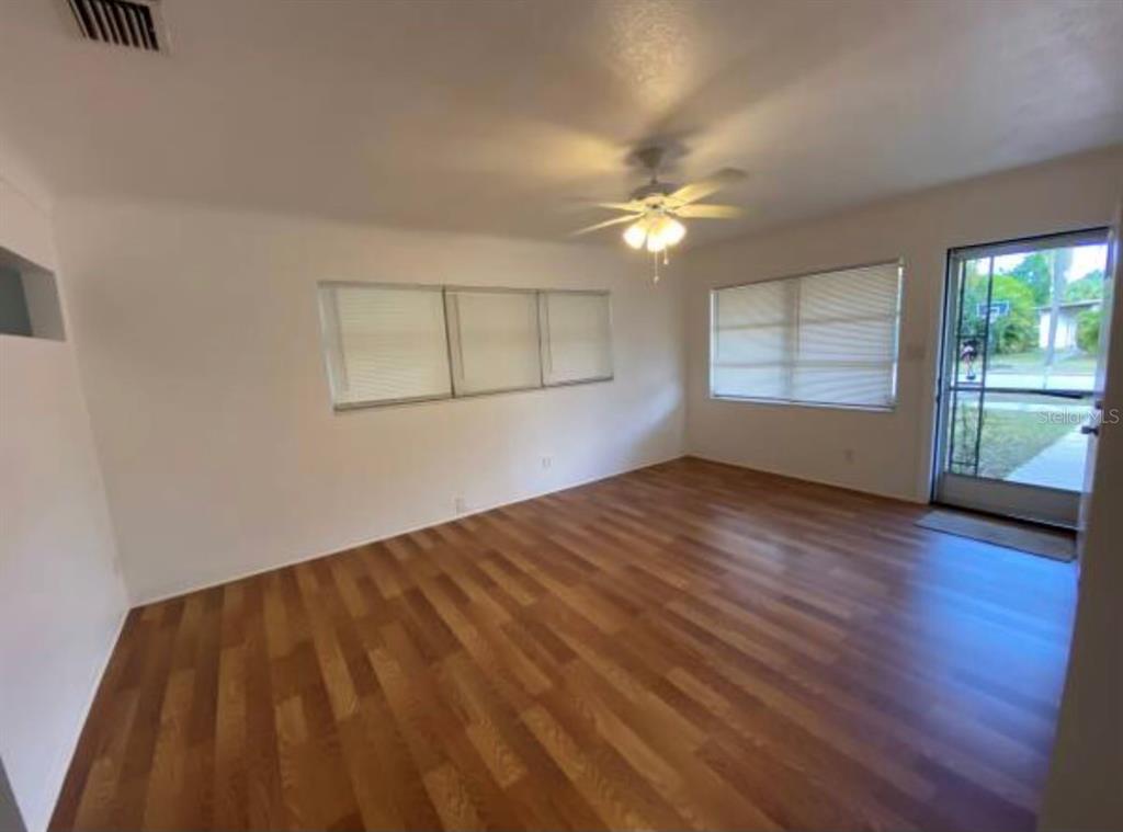 An empty living room features wood-look flooring, a ceiling fan, and windows with white blinds — 5744 2ND AVENUE N, ST PETERSBURG, FL