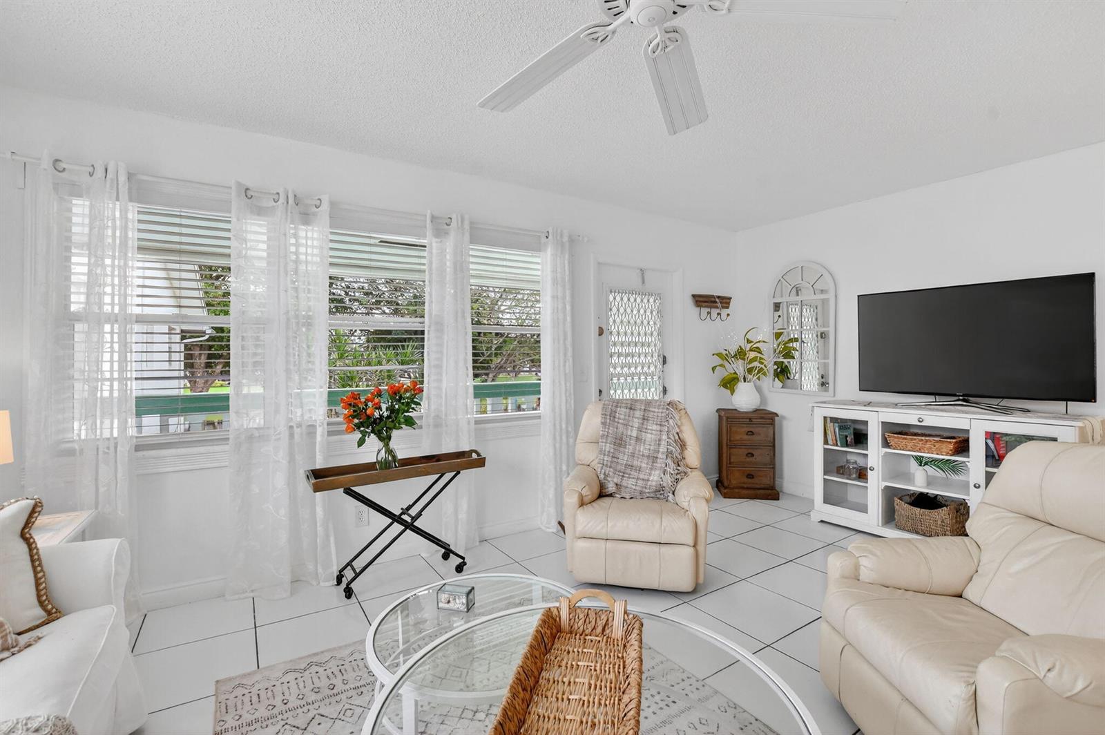 A bright living room features white tile floors, a ceiling fan, and a television console — 477 Tilford V, Deerfield Beach FL 33442, DEERFIELD BEACH, FL