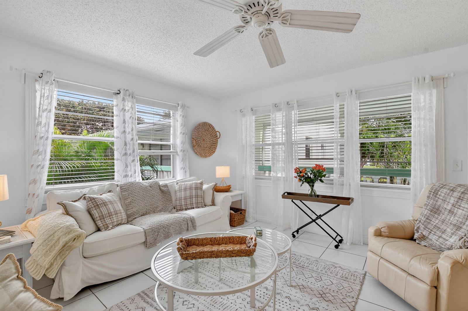 A bright living room features white furniture, glass coffee tables, tile floors, and large windows — 477 Tilford V, Deerfield Beach FL 33442, DEERFIELD BEACH, FL