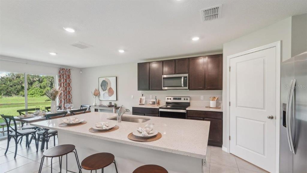 A kitchen with dark cabinets, a large quartz island, and a dining area with backyard views — 15015 CROSSHALL STREAM DRIVE, WIMAUMA, FL