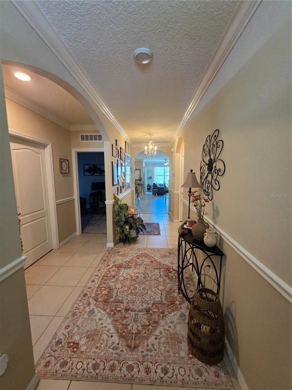 A tiled hallway features an arched entryway, a decorative rug, and a console table — 1762 BROCKRIDGE ROAD, KISSIMMEE, FL