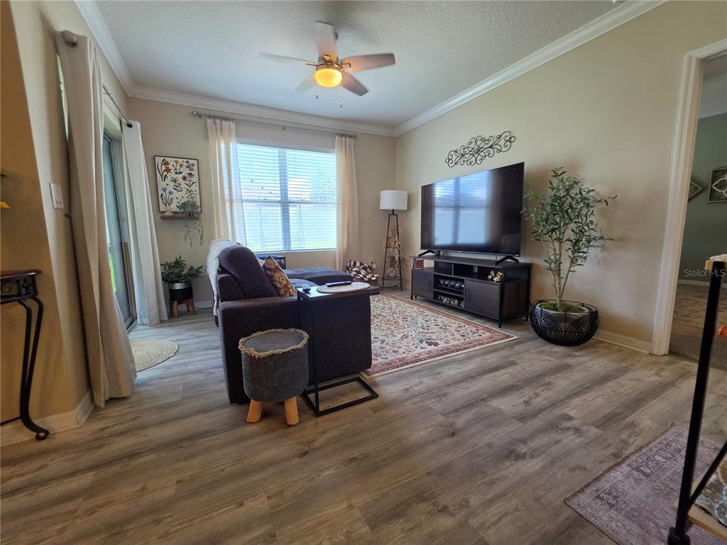 A living room features wood-look flooring, a large television, a sofa, and a ceiling fan — 1762 BROCKRIDGE ROAD, KISSIMMEE, FL