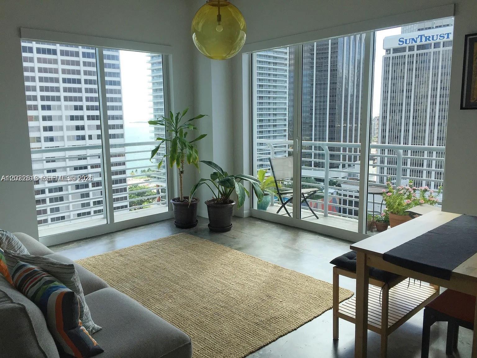 A living room with concrete floors, a jute rug, and floor-to-ceiling windows overlooking city buildings — 133 NE 2nd Ave # 2302, Miami FL 33132, MIAMI, FL