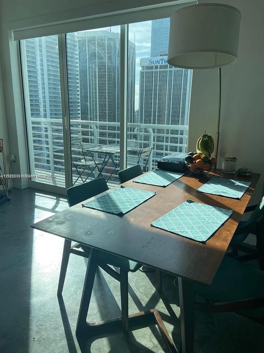 A dining area features a wooden table with placemats and a balcony overlooking city skyscrapers — 133 NE 2nd Ave # 2302, Miami FL 33132, MIAMI, FL