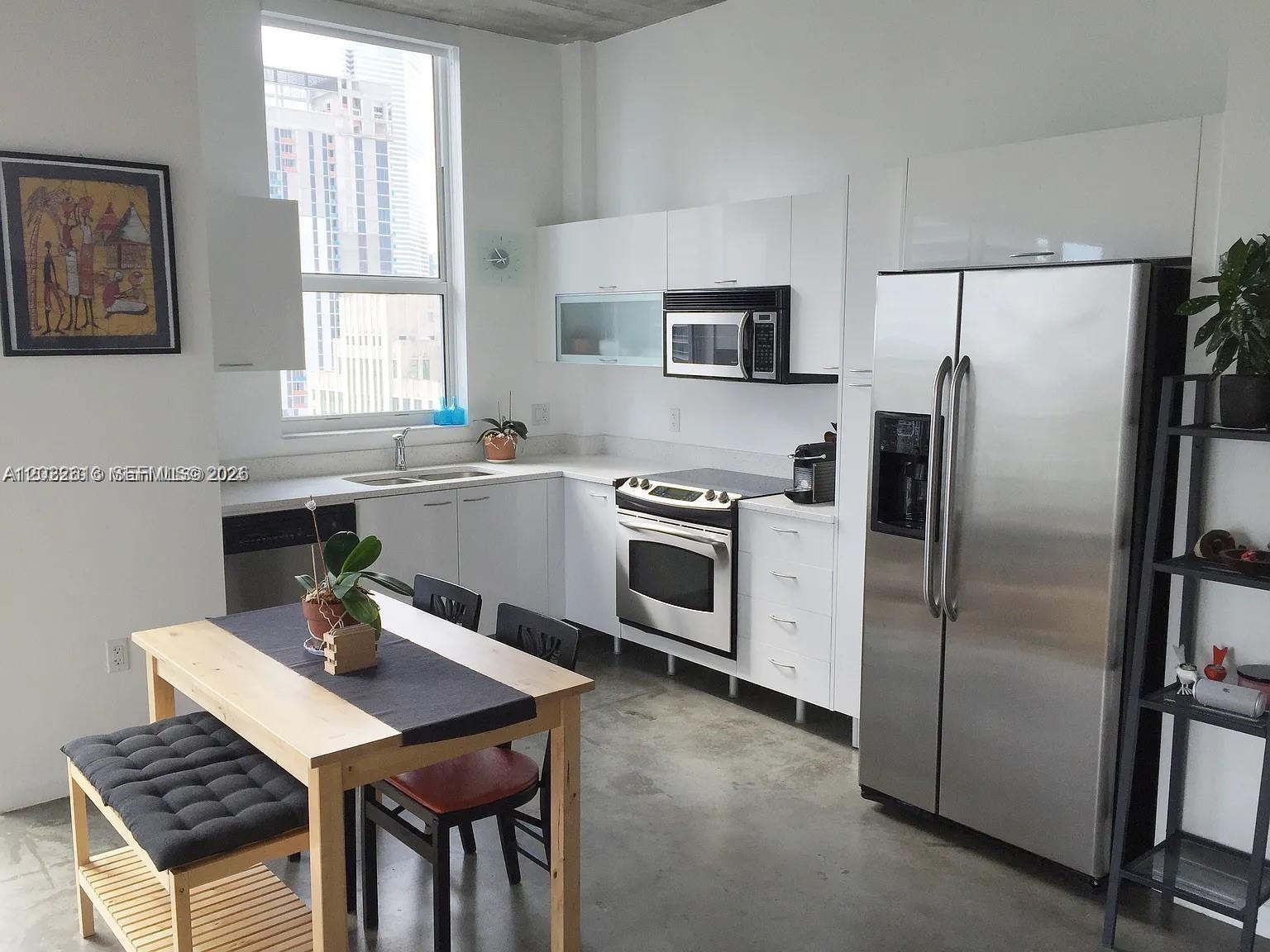 A modern kitchen features white cabinets, stainless steel appliances, and a dining table on concrete floors — 133 NE 2nd Ave # 2302, Miami FL 33132, MIAMI, FL