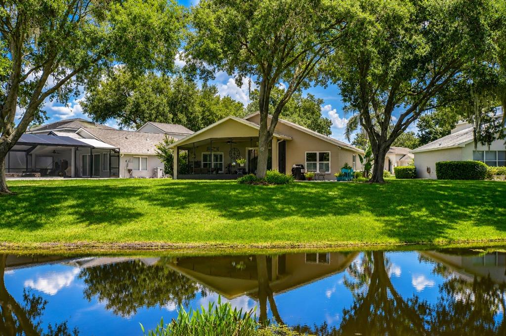 A tan house with a screened-in lanai sits behind a grassy lawn and a pond — 5616 ROCKFIELD LOOP, VALRICO, FL