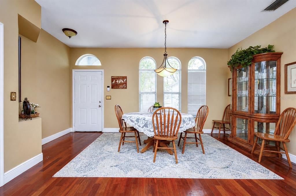 A dining room features a round table, wooden chairs, a china cabinet, and hardwood floors — 4102 AMBER RIDGE LANE, VALRICO, FL