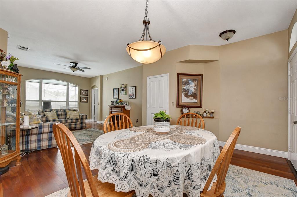 A dining area with a round table, wooden chairs, and hardwood floors opens to a living room — 4102 AMBER RIDGE LANE, VALRICO, FL