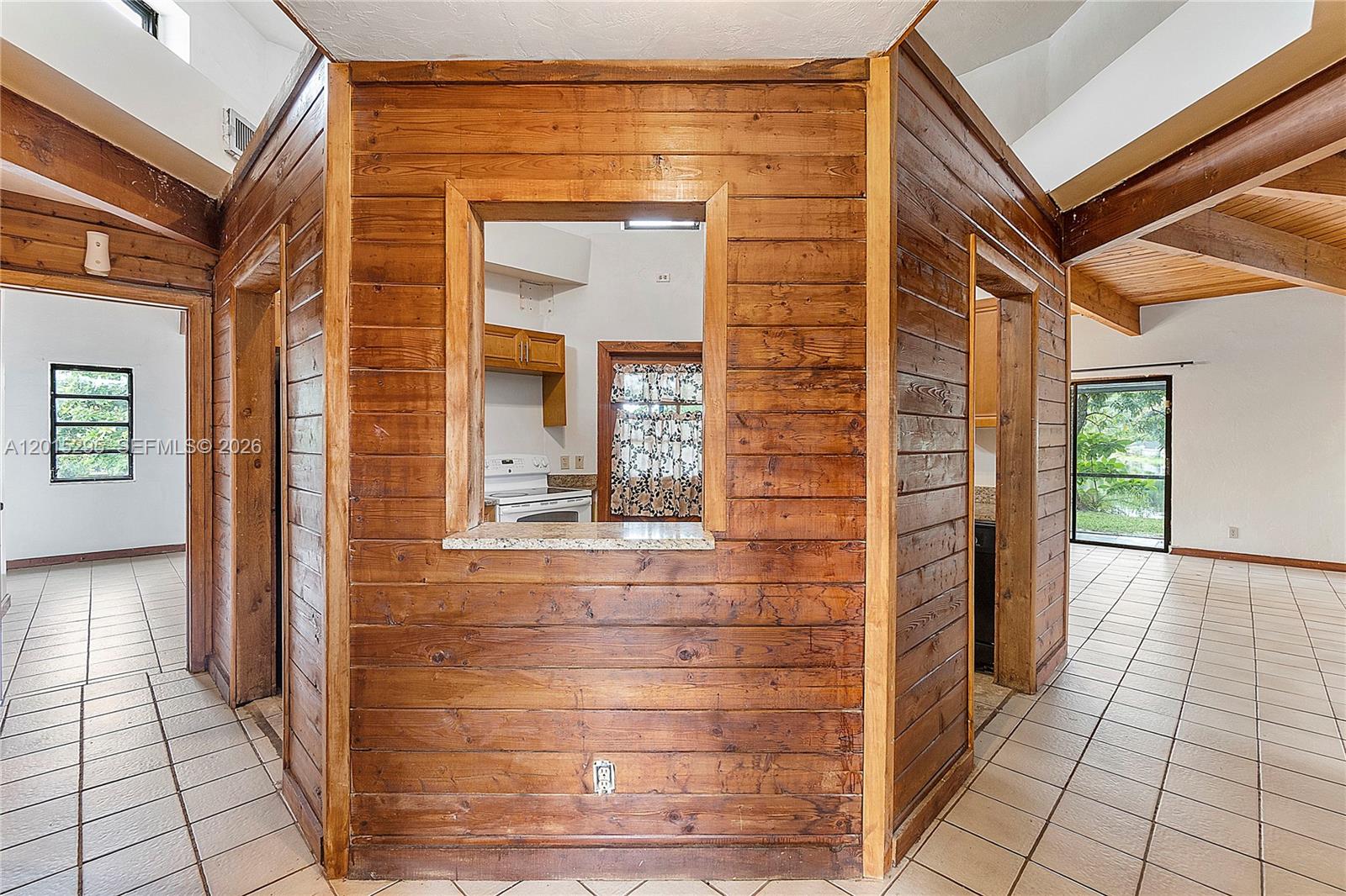 A central wood-paneled wall features a pass-through window looking into a kitchen — 4561 NW 79th Ave, Lauderhill FL 33351, LAUDERHILL, FL