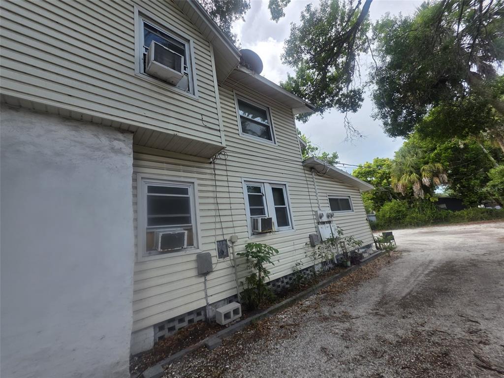 The exterior of a two-story house features light-colored siding, multiple window air conditioning units, and gravel — 602 W 26TH STREET, BRADENTON, FL