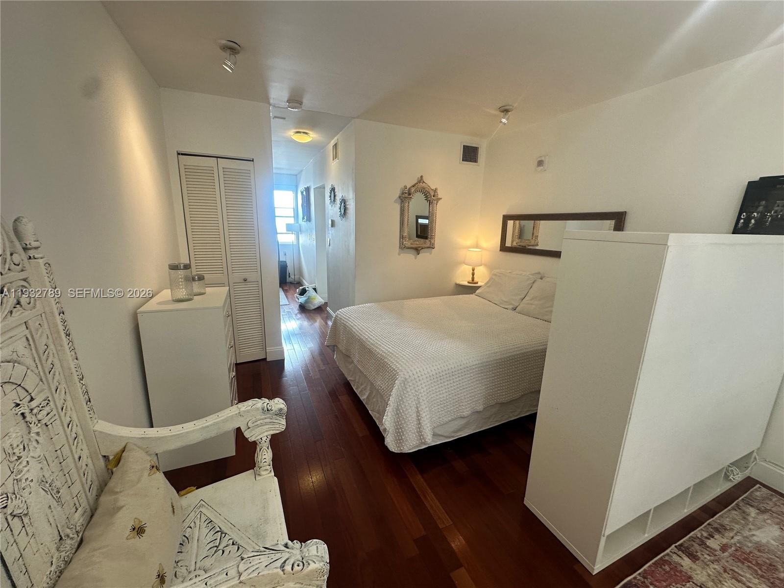 A bedroom features a bed, white furniture, a decorative chair, and dark wood flooring — 1340 Drexel Ave # 406, Miami Beach FL 33139, MIAMI BEACH, FL