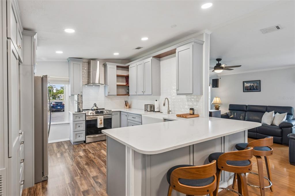 A modern kitchen features light gray cabinets, white countertops, and an island with bar stools — 276 PELICAN DRIVE N, OLDSMAR, FL