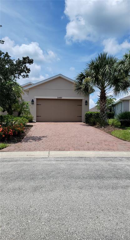 A tan house with a two-car garage and a paved driveway under a blue sky — 3497 FALLBROOK DRIVE, KISSIMMEE, FL