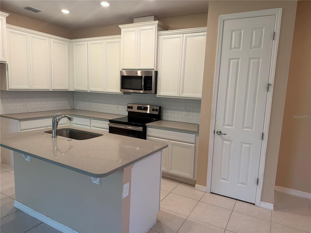 A kitchen features white cabinets, stainless steel appliances, a center island, and light-colored countertops — 3497 FALLBROOK DRIVE, KISSIMMEE, FL