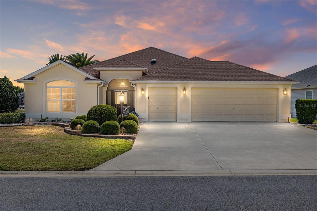 A single-story house with a three-car garage and landscaped front yard at sunset — 1440 ALESIO STREET, THE VILLAGES, FL